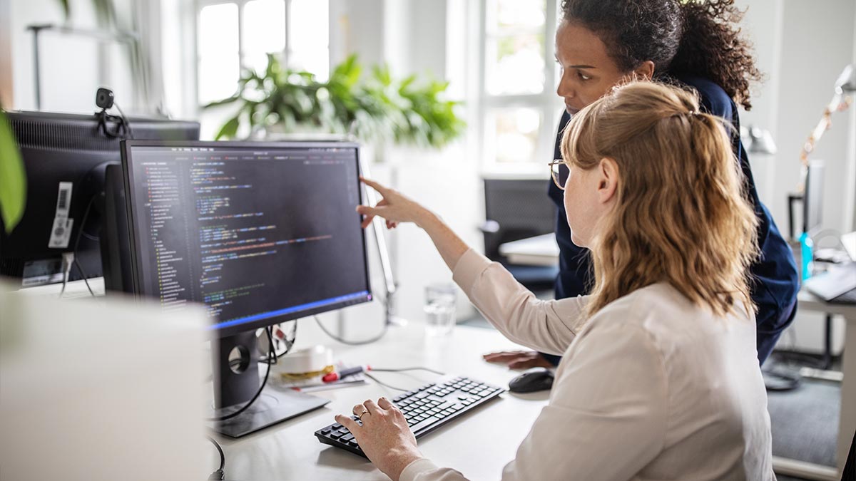 Two women sat at a desk looking at data on a computer screen